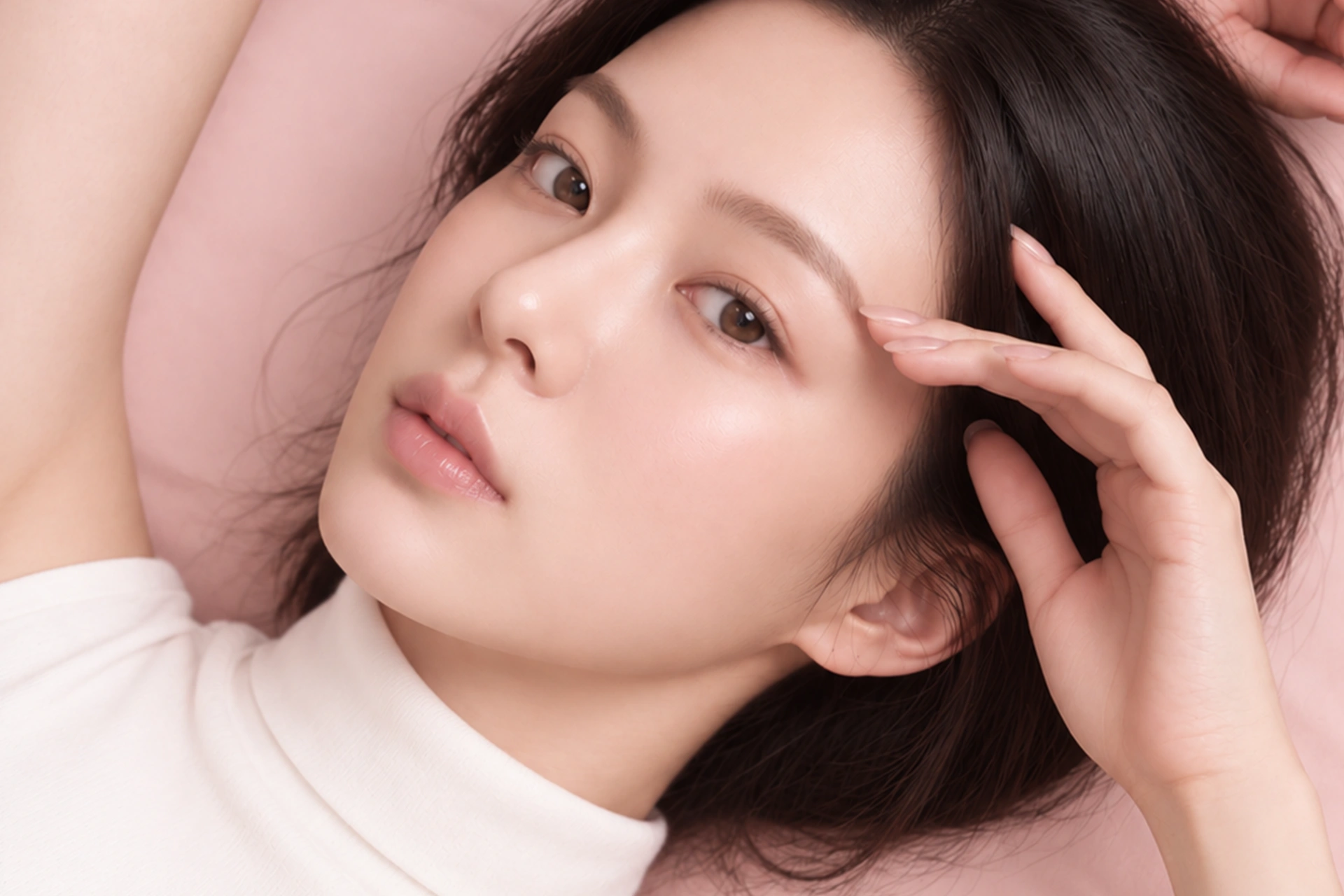 연한 핑크 배경에서 얼굴과 손을 담은 뷰티 모델 연출 이미지
